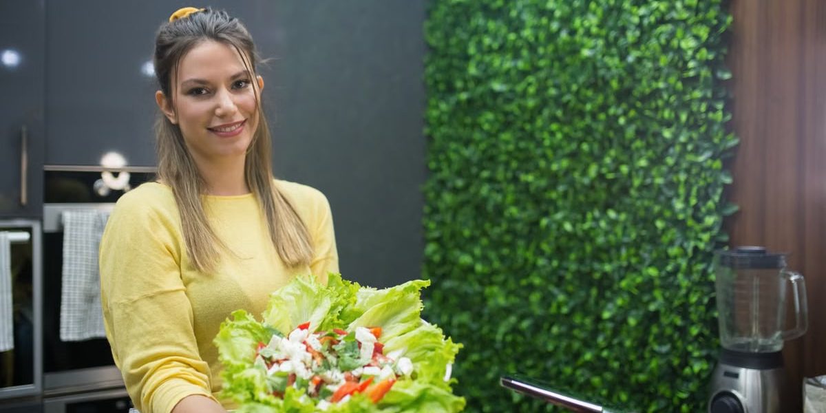 A cheerful woman in a modern kitchen presenting a fresh vegetable salad.